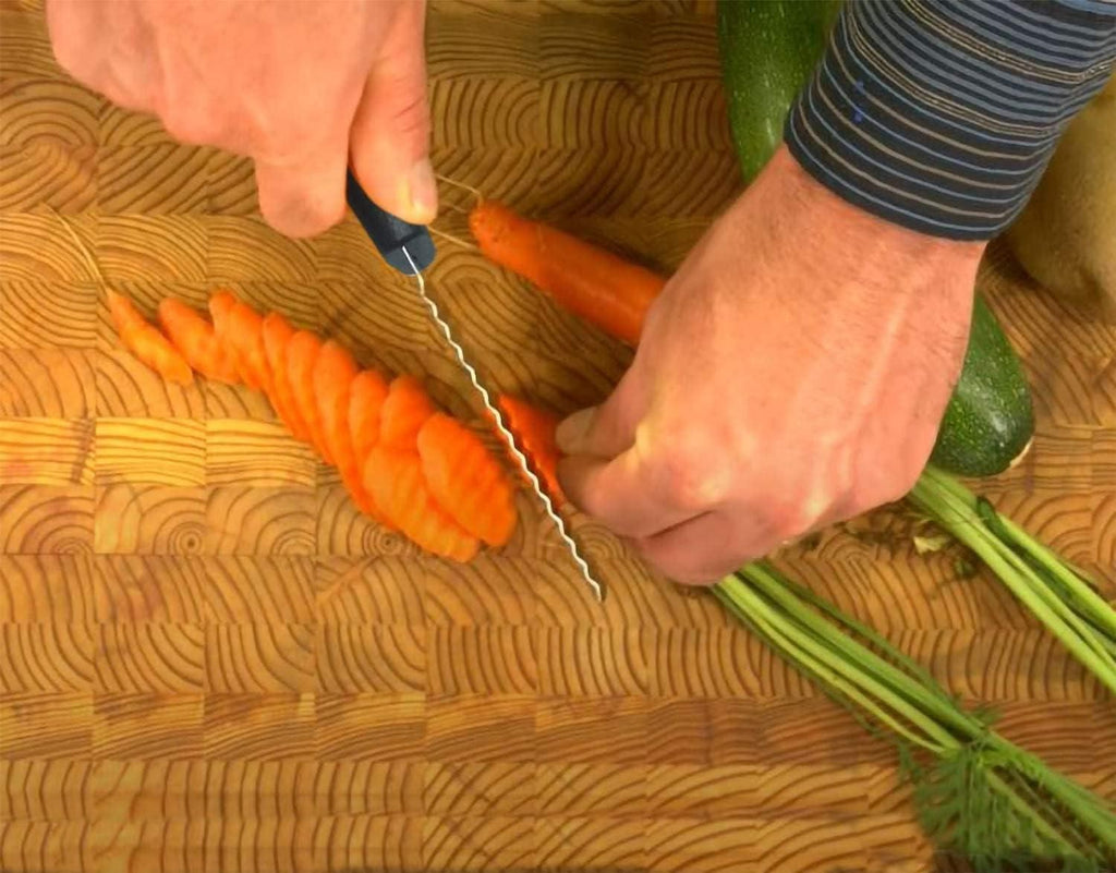 Person cutting carrots on a wooden cutting board with a knife.