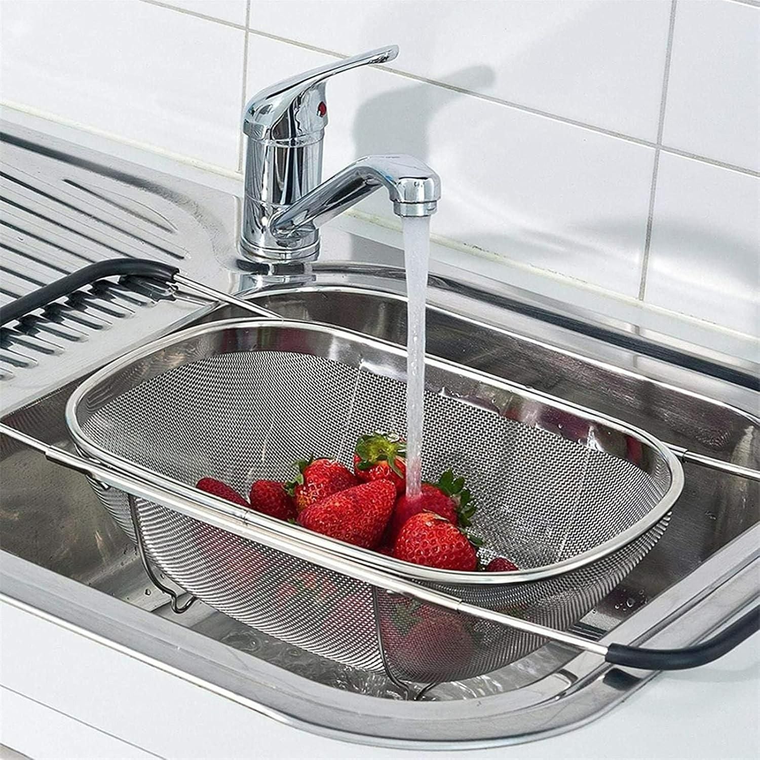 Strainer with strawberries being rinsed under running water in a kitchen sink.