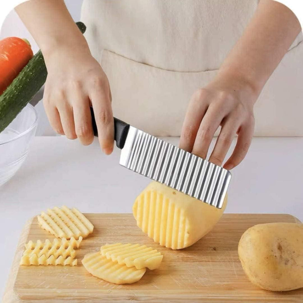 Person using a potato peeler to create wavy slices on a wooden cutting board with vegetables in the background.