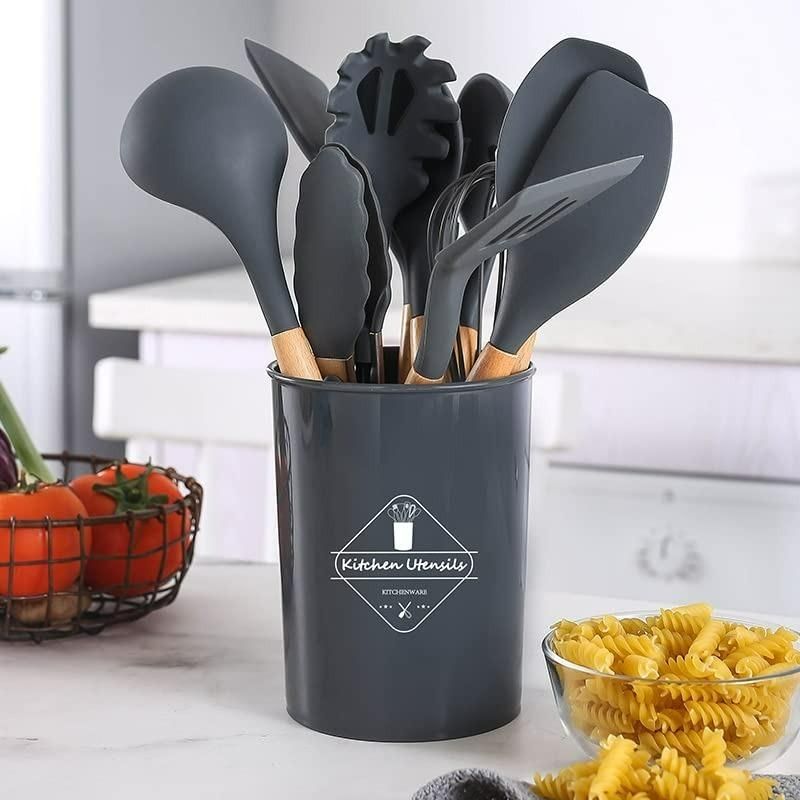 Set of black kitchen utensils in a holder on a kitchen counter with pasta and tomatoes.