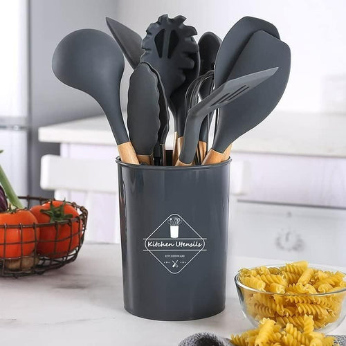 Set of black kitchen utensils in a holder on a kitchen counter with pasta and tomatoes.